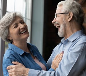 Happy older couple laughing together indoors, emphasizing joy and connection, relevant to maintaining comfort and positivity during winter recovery after dental implant surgery.
